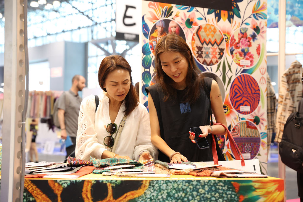 Two attendees examining fabric samples at a booth with colorful textile designs at Texworld New York.